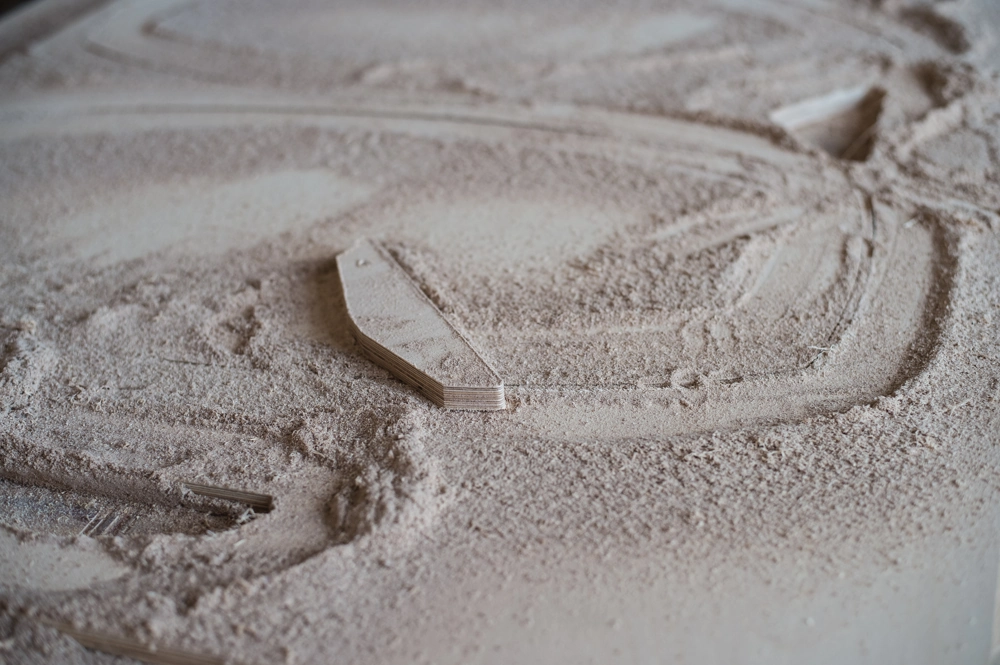 Stół do obróbki drewna z resztkami sklejki i obficie pokryty drobnym pyłem drzewnym